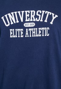 Camiseta de algodón azul marino con texto blanco: "UNIVERSIDAD FUNDADA EN 1991 ATLÉTICO ELITE." Textura suave con un clásico escote redondo.