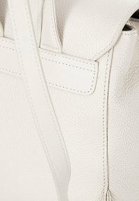 Zaino in pelle bianca con finitura testurizzata, cuciture a contrasto e spallacci regolabili. Presenta una chiusura a patta e tasche laterali.