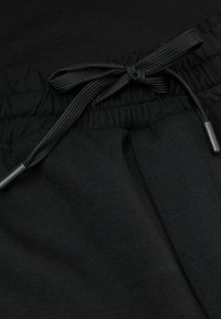 Czarne dresy z elastycznym paskiem z sznurkiem, matową fakturą i gładką powierzchnią. Sznurek ma czarne plastikowe końcówki.