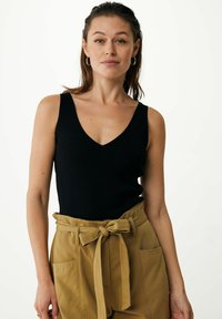 Schwarzes, geripptes Tanktop mit V-Ausschnitt, kombiniert mit hoch taillierten, olivgrünen, mit Gürtel versehenen Hosen mit Seitentaschen.
