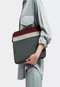 Housse d'ordinateur portable en vert foncé avec des rayures bordeaux et beige. Matériau texturé, design fin avec fermeture éclair et bords doux.