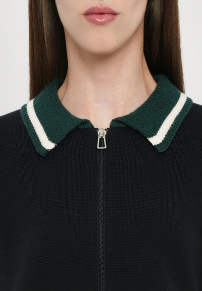 Geacă neagră cu fermoar, având un design texturat din tricot, cu un guler verde accentuat de două dungi albe.