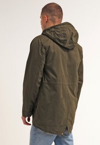 Olivgrön lättviktsjacka med huva och slät textur samt justerbar huva. Har sidofickor och en knappdetalj vid bakfållen.