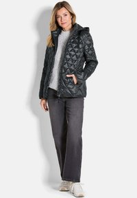 Veste noire matelassée avec capuche, fermeture zippée, poches latérales, et pull gris en dessous. Assortie avec un jean noir et des baskets blanches.