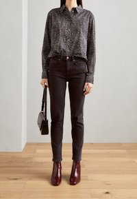 Mustavalkoinen pilkullinen nappipaita yhdistettynä tummiin kapealahkeisiin farkkuihin ja viininpunaisiin nilkkureihin, kädessä pieni musta olkalaukku.