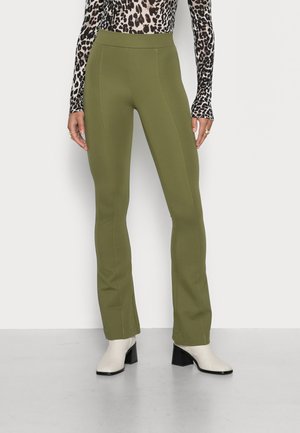 Calças ajustadas verde-oliva com cintura alta e detalhes de costura limpos, combinadas com botas de tornozelo de salto bloco em creme. Textura suave.