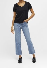 T-shirt noir à manches courtes et col en V avec une poche sur la poitrine, associé à un jean en denim clair évasé et des mocassins noirs.