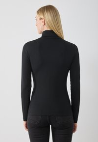 Must have musta varrukatega turtleneck top pehmest kangast, sobiv disain, millel on kõrge krae ja sile tekstuur, koos tumsiniste denimist teksadega.