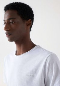 Camiseta blanca de manga corta con cuello redondo, de material de algodón, que presenta un sutil logo bordado de "Salsa Jeans" en el pecho izquierdo.