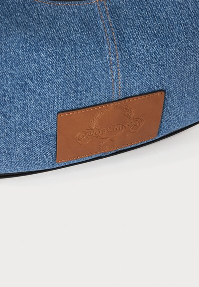 Μπλε denim ύφασμα με πορτοκαλί ραφές και καφέ δερμάτινο ταμπελάκι με ανάγλυφο το λογότυπο Moschino και το κείμενο Milano.