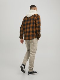 Checkered brown and black flannel shirt with a white hood, beige cargo pants, and black sneakers. Textured fabric, relaxed fit, casual style.