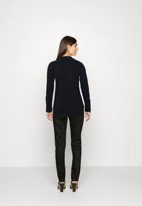 Zwarte lange mouwen shirt met een ronde halslijn, lichte stof en een aansluitend ontwerp, gecombineerd met zwarte tapered broek en hakken.