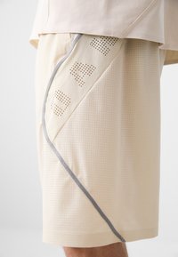 Beige shorts made of textured fabric with a diagonal design featuring perforated accents and a grey trim along the side.