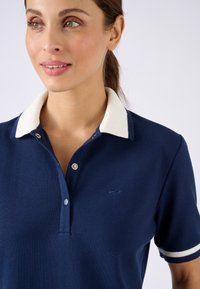 Polo navy avec un col et des accents de manches côtelés blancs. Doté d'un tissu texturé et d'une patte de boutonnage à trois boutons avec des boutons en argent.