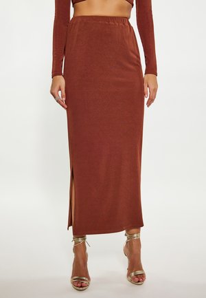 Bruine geribbelde maxi rok met een elastische tailleband en een split aan de zijkant. Gecombineerd met metallic hakken met bandjes, wat een slanke silhouette benadrukt.