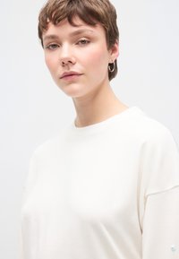 Λευκό βαμβακερό φούτερ με άνετη γραμμή, στρογγυλή λαιμόκοψη και χαμηλωμένους ώμους. Μικρή κεντητή λεπτομέρεια στο μανίκι.