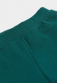 Detailní záběr na modrozelený elastický ribbovaným pás na látkových kalhotách nebo šortkách se shromážděným švem pod pásem.