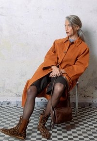 Cappotto arancione oversize, gonna scura, stivali in nappa con stampa leopardata e borsa in pelle marrone. Texture lisce e modelli contrastanti.