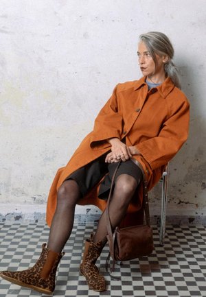 Oranžový oversized kabát, tmavá sukně, semišové boty s leopardím vzorem a hnědá kožená kabelka. Hladké textury a kontrastní vzory.