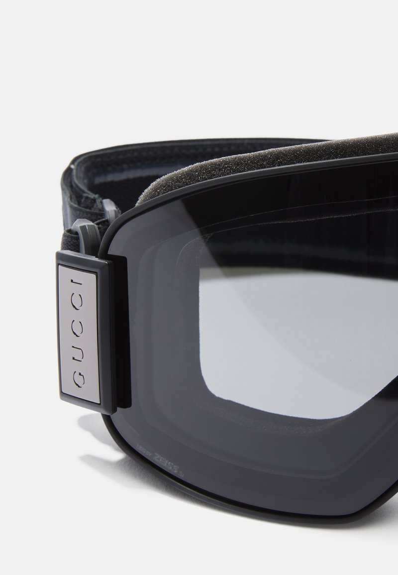 Black ski goggles with a soft foam lining and adjustable strap. Features a silver logo on the side and curved, tinted lenses.