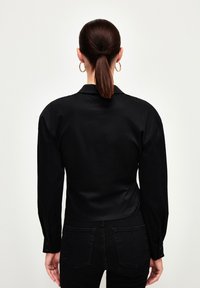 Sort skjorte med lange ærmer, glat tekstur og klassisk krave. Bæres med sorte højtaljede jeans.