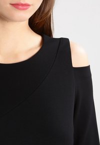 Schwarzes schulterfreies Oberteil mit abgerundetem Ausschnitt, aus weichem Stoff, mit glatter Textur und minimalistischem Design.