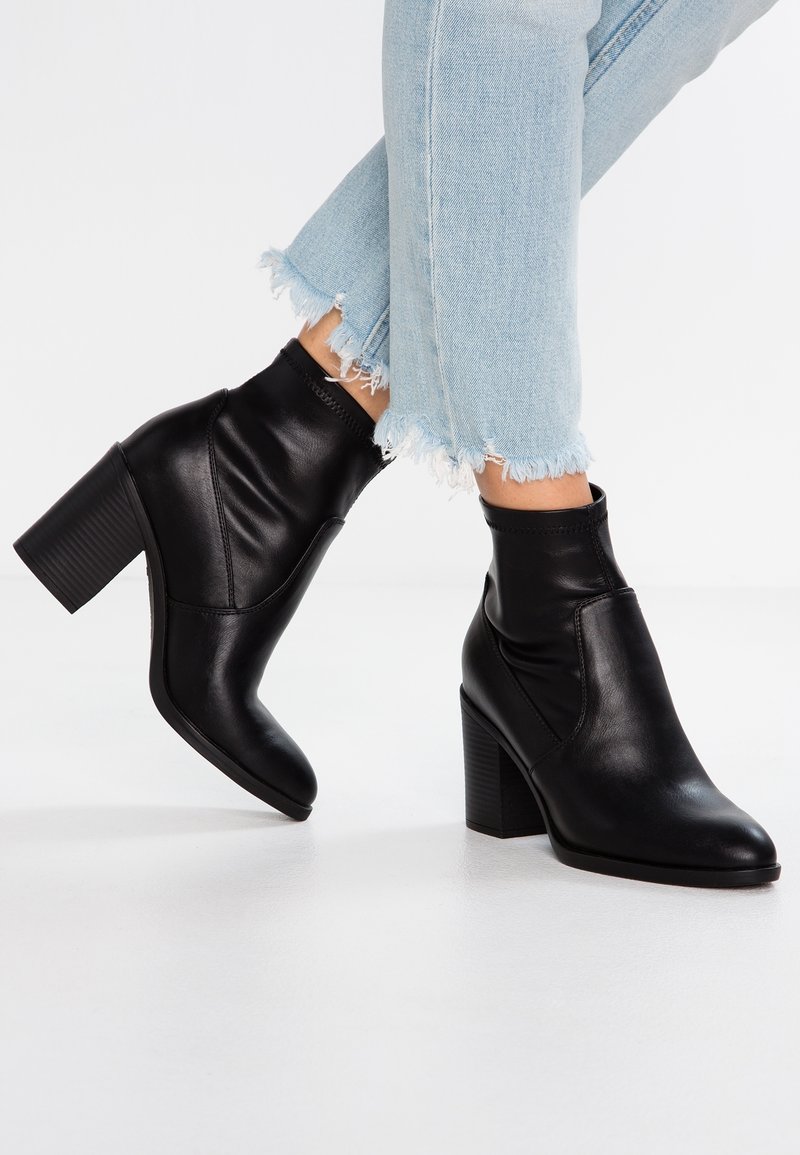 Bottes noires en cuir jusqu'à la cheville avec une finition lisse, un bout pointu et un talon bloc texturé. Les jeans présentent un ourlet effiloché pour un look décontracté.