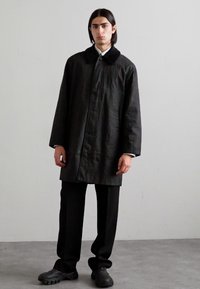 Cappotto nero oversize con colletto, maniche lunghe e silhouette dritta. Abbinato a pantaloni neri a gamba dritta e scarpe nere chunky.