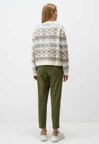 Knitted sweater with a geometric pattern in beige, light blue, and brown. Paired with olive green trousers and white sneakers.