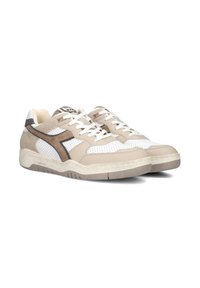 Sneaker beige e bianche con texture perforata, dettagli in suede e lacci piatti. Presentano un logo marrone scuro a contrasto e una suola in gomma.