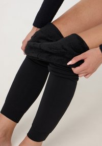 Pantaloni neri in stile leggings con una morbida e pelosa consistenza nella parte superiore, raccolti e arrotolati, che mettono in mostra un design della gamba inferiore elegante e liscio.