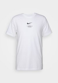 Vit bomullströja med korta ärmar, som har en svart Nike-logga och text på framsidan. Enkel design med rundad halsringning.