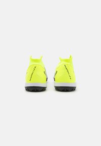 Zapatillas deportivas en un brillante color amarillo con un diseño de tobillo ceñido. Presentan acentos negros y una suela texturizada para un mejor agarre. Branding minimalista visible.