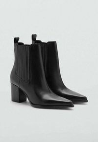 Botines de cuero negro con punta estrecha, paneles laterales elásticos acanalados y tacón grueso. Cuenta con tiradores en la parte trasera para facilitar su uso.