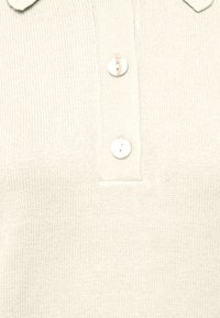 Cremfarbener, gestrickter Poloshirt mit strukturiertem Stoff, einem Kragen und zwei Knöpfen auf der Vorderseite. Einfaches und sauberes Design.
