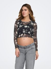 Musta läpikuultava pitkähihaisen lyhyt yläosa kukkakuvioin, yhdistetty harmaisiin joustavaan vyötäröön oleviin housuihin. Helma on aaltoileva.