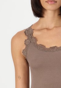 Débardeur marron côtelé avec une bordure en dentelle le long de l'encolure. Le tissu est doux avec une apparence texturée, et possède des bretelles réglables.