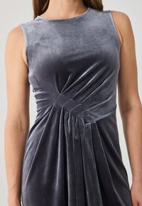 Šedé sametové šaty bez rukávů s předními záhyby, které mají hladkou texturu a kulatý výstřih. Látka se elegantně splácí.