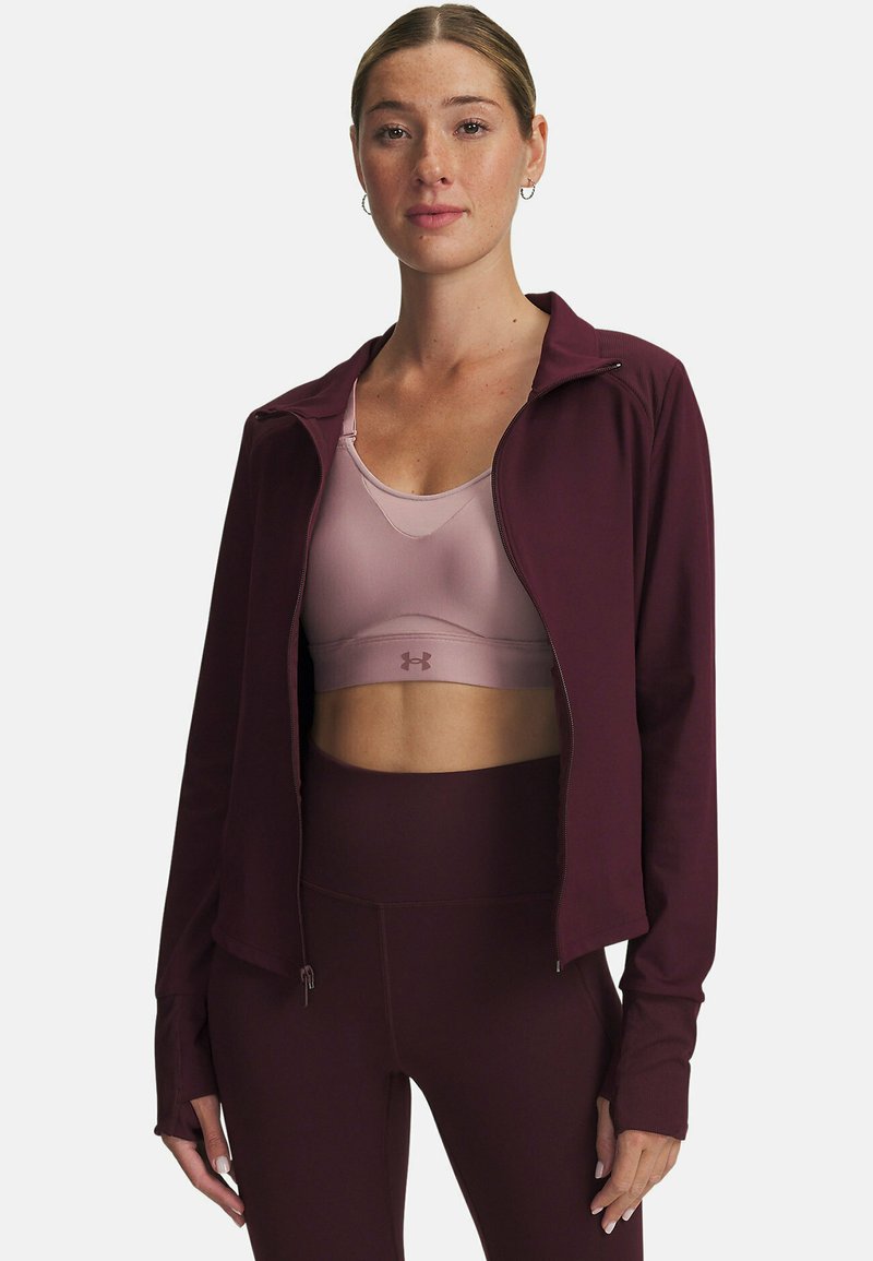 Maroon Zip-Jacke mit Reißverschluss, die über einem hellrosa Sport-BH getragen wird, ergänzt durch hochtaillierte, kastanienbraune Leggings mit glatter Textur und figurbetontem Schnitt.