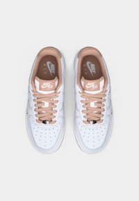 Une paire de baskets Nike Air Force 1 blanches avec des lacets et une doublure intérieure marron clair, vues de dessus sur un fond blanc uni.