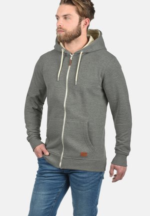 Grijze rits-hoodie met een khaki binnenkant, trekkoordcapuchon, voorzakken en een leren logo-patch. Zacht materiaal met een relaxte pasvorm.