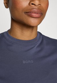 Tums zils kokvilnas krekls ar apaļu kaklu un smalku "BORG" tekstu logotipu, izdrukātu gaišākā tonī. Gluda tekstūra ar minimālismu dizaina detaļās.