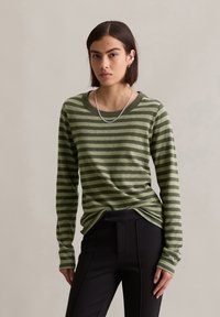 Groen en donkergroen gestreepte blouse met lange mouwen, een wijde halslijn en aansluitende mouwen, gecombineerd met zwarte broek. Gestructureerde stof.
