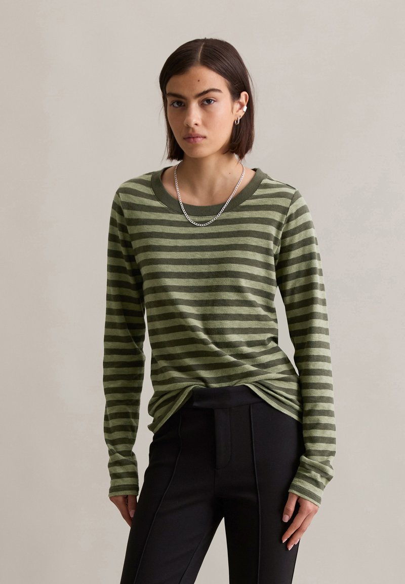 Groen en donkergroen gestreepte blouse met lange mouwen, een wijde halslijn en aansluitende mouwen, gecombineerd met zwarte broek. Gestructureerde stof.