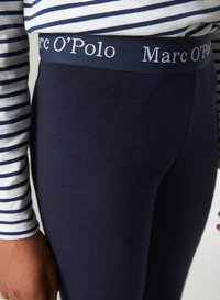 Marineblauwe leggings met een zachte textuur en een brede tailleband met het witte "Marc O’Polo" logo. Gestreepte lange mouwen shirt zichtbaar erboven.
