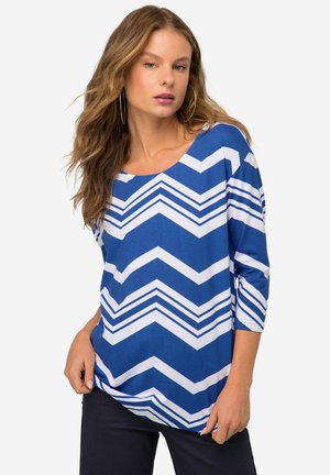 Bluse mit blau-weißer Zickzackmusterung, dreiviertel Ärmel und runder Ausschnitt, aus einem glatten Textilmaterial gefertigt.
