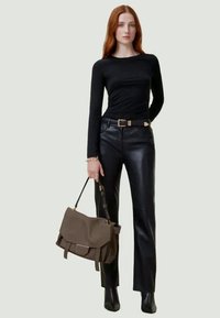 Camisola preta de manga longa combinada com calças de couro de cintura alta. Mala castanha com abas, segurada numa mão. Botas pretas de cano curto.