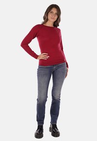 Maglione rosso a maniche lunghe realizzato in un materiale morbido e liscio. Abbinato a jeans blu e stivali neri con lacci, presenta un colletto rotondo e un design aderente.