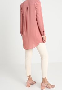 Långärmad blus i puderrosa med en rundad nederkant. Kombinerad med vita jeans med fransade ärmslut och rosa perforerade blockklackskor.