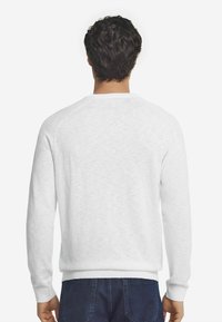 Weißes Sweatshirt mit strukturiertem Finish, gerippten Bündchen und Saum sowie Raglanärmeln. Getragen mit marineblauen Jeans. Rückansicht.